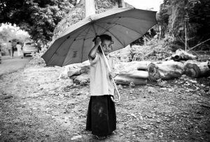 Title: Room for One More Photographer: Benjamin James Location: LAMP Mission, Nakkapali, Andra Pradesh, India. 2015 Description: A girl stands under an umbrella – twice her size – at the LAMP Mission Home. Through Kitechild, the home was able to reconstruct their roof to protect the sleeping area for the children from the common rains. 